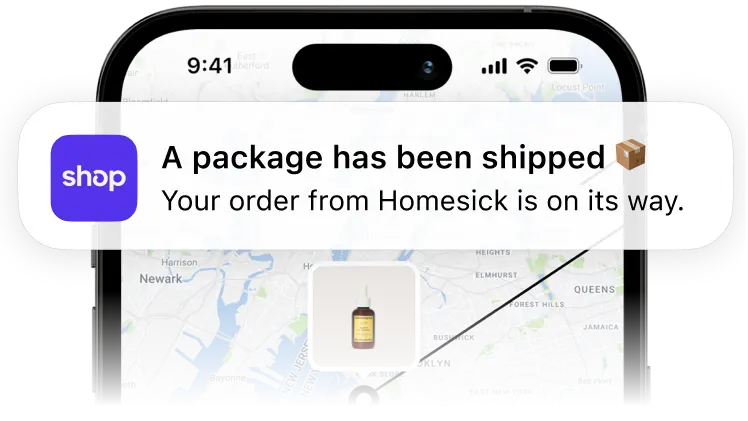 A mobile phone displaying a notification from the Shop app that a package from Homesick has been shipped with a tracking map behind it