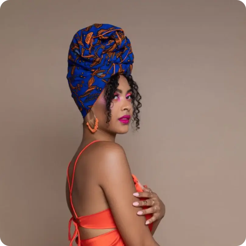 A woman wearing an orange top, a colorful headwrap, and bright makeup