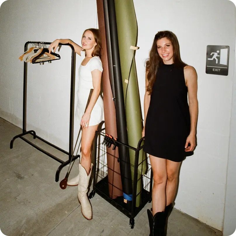Two women, one wearing a white golf dress and holding a golf club, the other wearing a black golf dress, smiling at the camera
