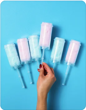 Several blue and pink cotton candy sticks are laid out on a blue surface. A person’s hand is in frame, holding one of them.