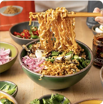 A bowl of ramen noodles. A person’s hand holding chopsticks is in frame, getting a bite of ramen.