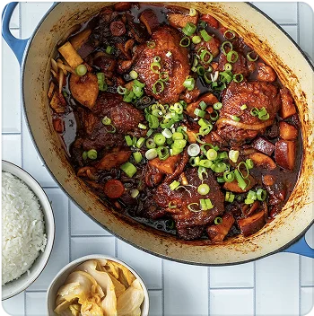 A large pot of food paired with white rice on a flat surface.