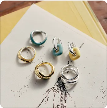Six pieces of various jewelry (some gold, silver, turquoise, and yellow) are laid out on a sketchpad.