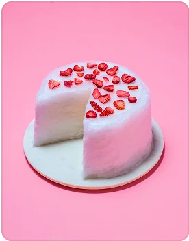 A pink cotton candy cake on a white plate on a pink background.