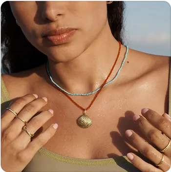 A close-up of a woman from the nose down, showing two necklaces: one red and gold, one blue.